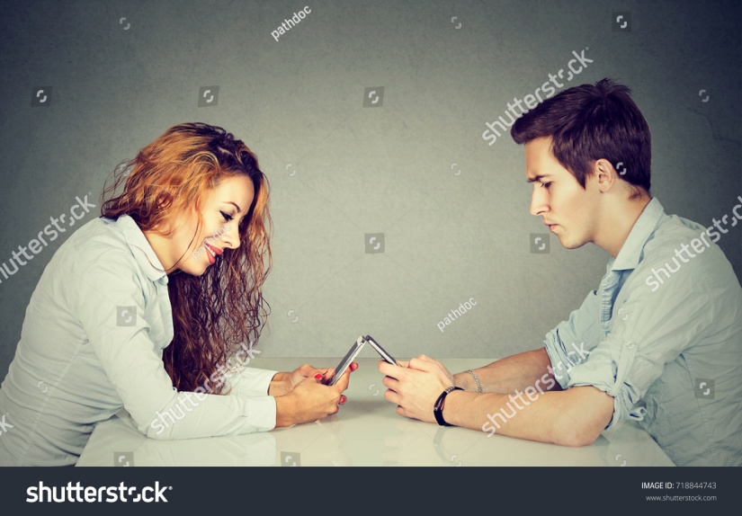 stock-photo-smartphone-addiction-concept-young-woman-and-man-sitting-at-table-with-smart-phone-ignoring-each-718844743